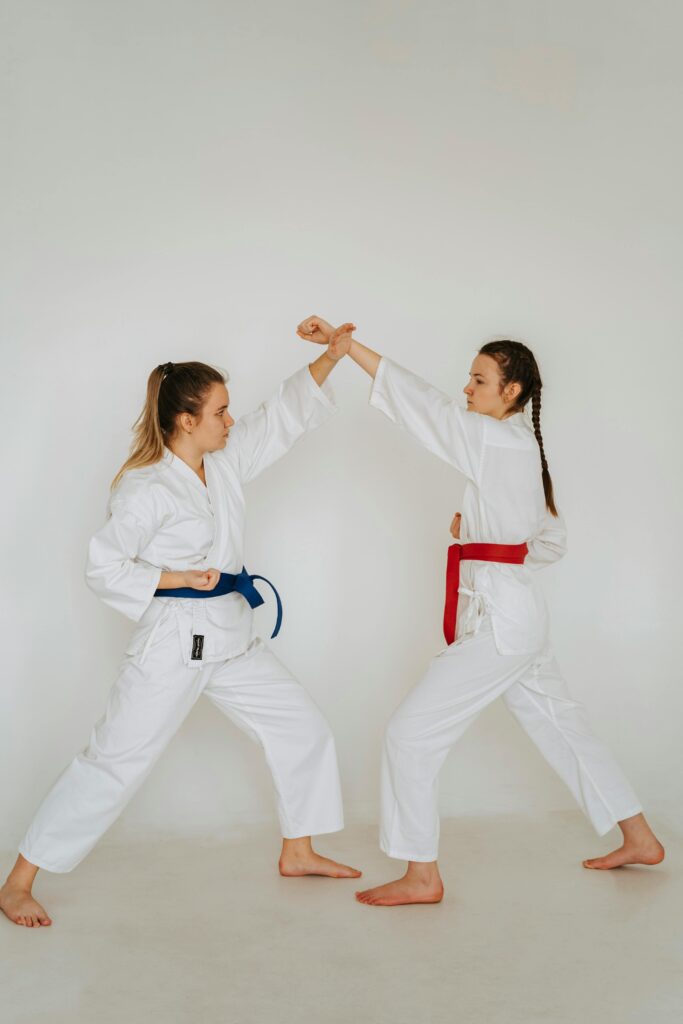 Two women in karate uniforms sparring in a bright studio setting.