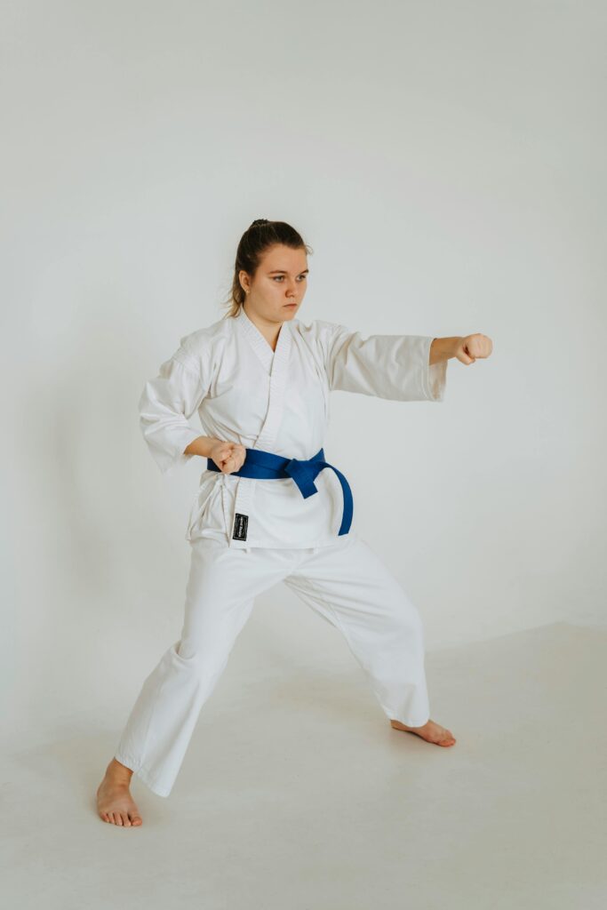 Woman practicing karate wearing a white gi with a blue belt, showcasing martial arts technique in studio.