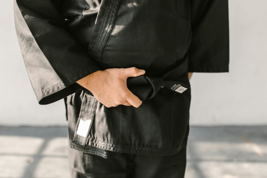 Close-up of a martial artist's hand holding a black belt in a judo uniform indoors.