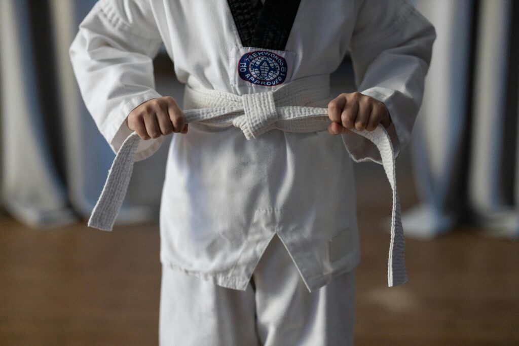 Close-up of a karate student tying a white belt in a traditional martial arts uniform.
